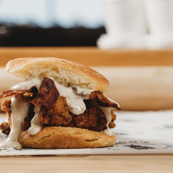 Lou Ann's Biscuits & Burgers' fried chicken and bacon biscuit sandwich, drizzled with white sauce.