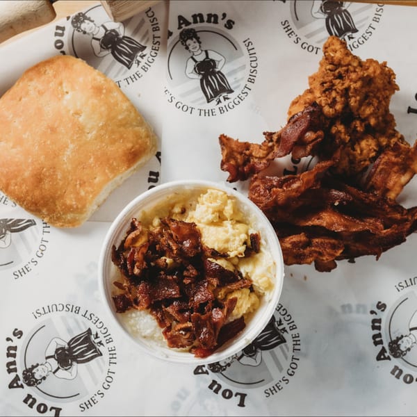 Lou Ann's breakfast with a biscuit, fried chicken, bacon, and a bowl of grits.