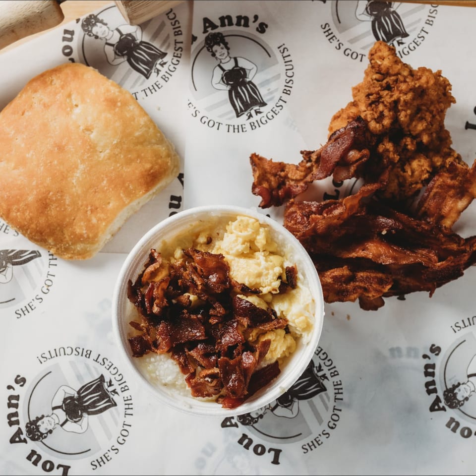 Lou Ann's breakfast with a biscuit, fried chicken, bacon, and a bowl of grits.